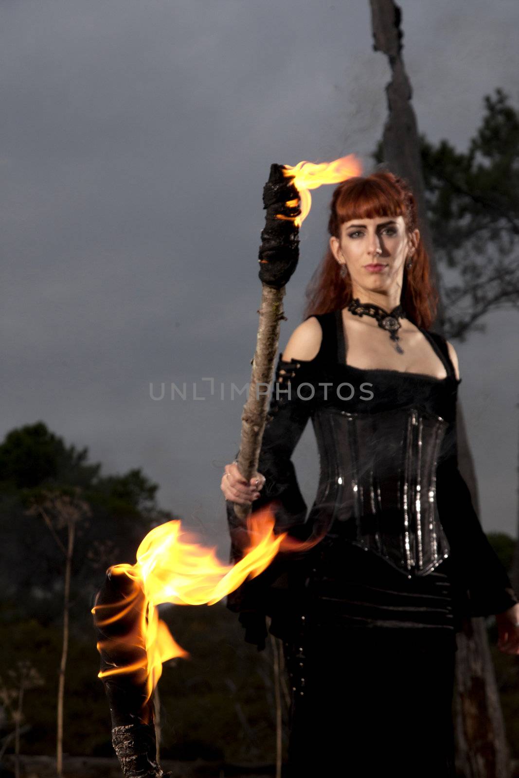View of a dark clothed woman with a torch on her hands.
