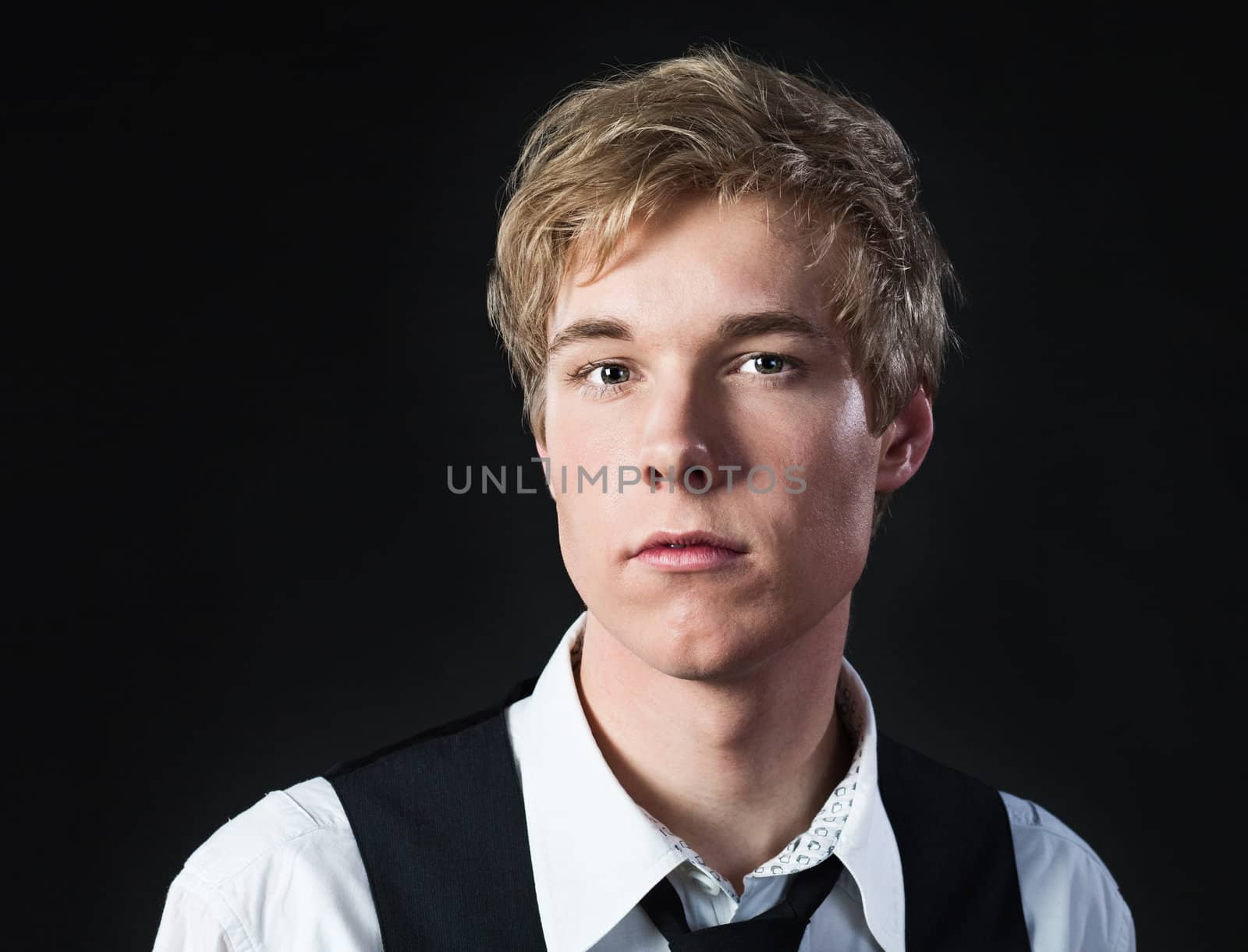 Portrait of serious young blond man in white shirt and waistcoat photographed against black background