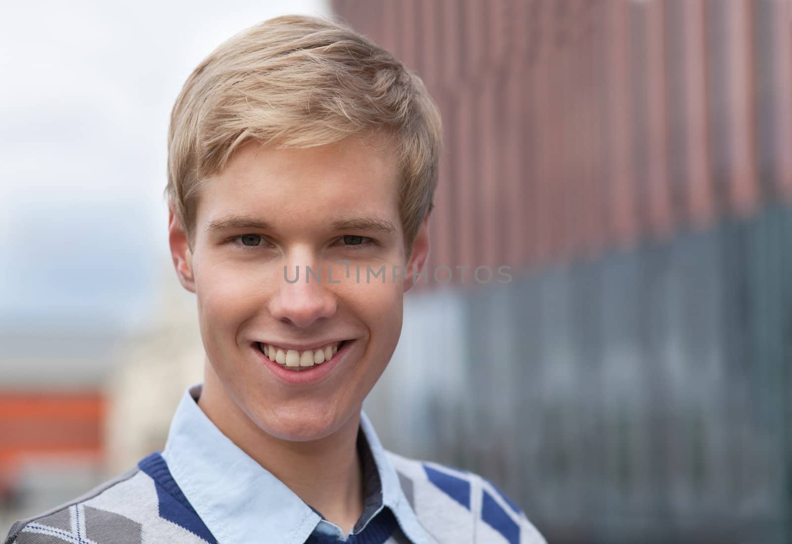 Handsome blond young man smiling outdoors; blurred background