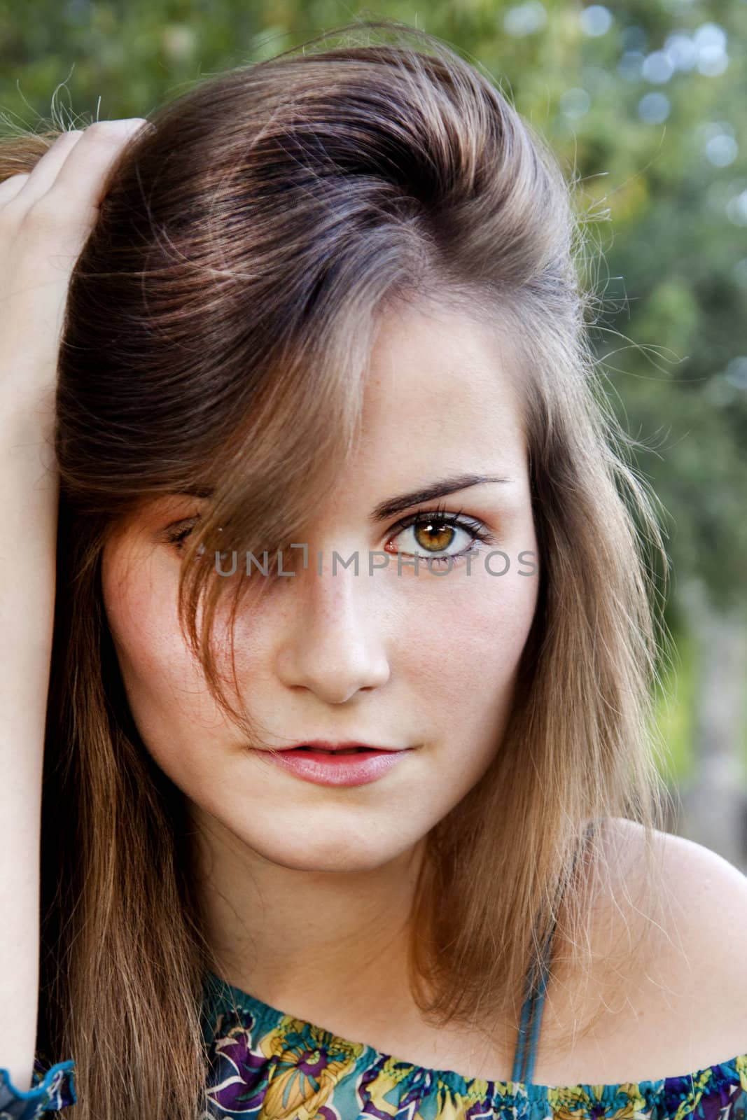 Closeup of the face of a beautiful young girl with hand on the hair.