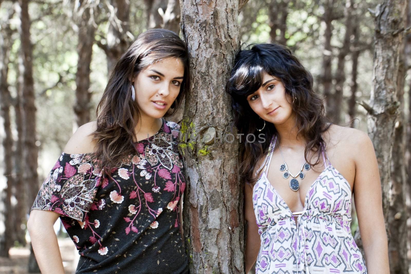 two girls pose next to a tree on the forest