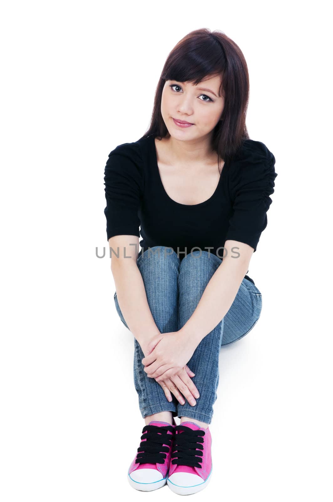 Portrait of a casual young woman sitting on floor over white background.