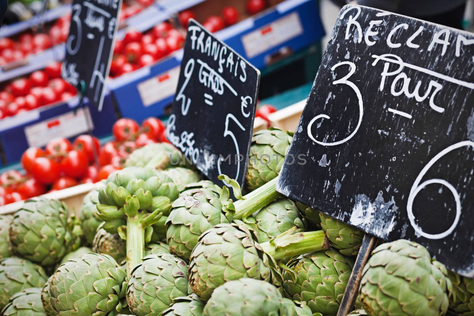 Closeup view on farm market counter with artichokes on the foreground; price tags in French