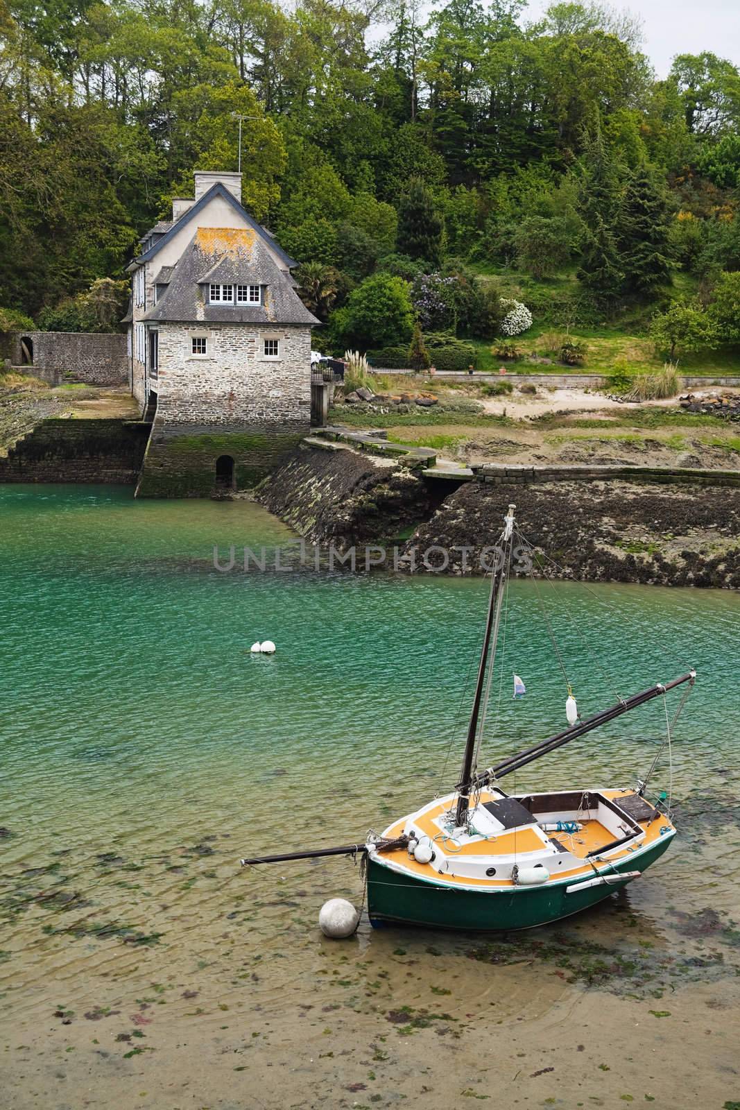 Colorful little yacht lying on the bottom at low tide near an old house