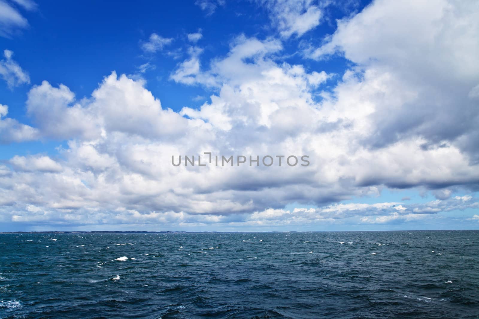 Sea ripples under cloudy sky; sea shore on horizon