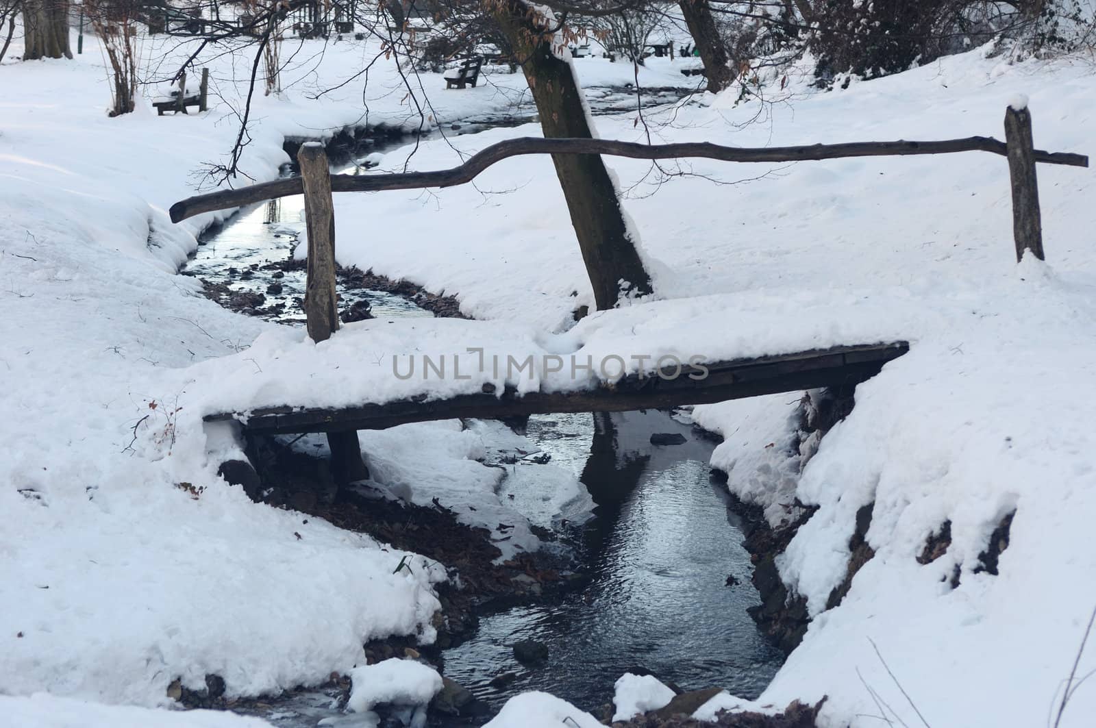Wooden bridge over small frozen brook with snow and ice