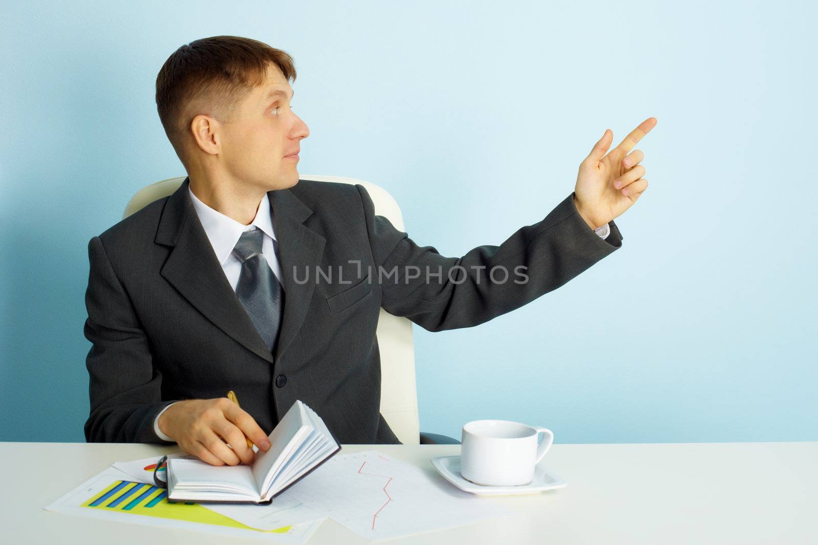 Business young man sitting at the table points a finger. Office scene
