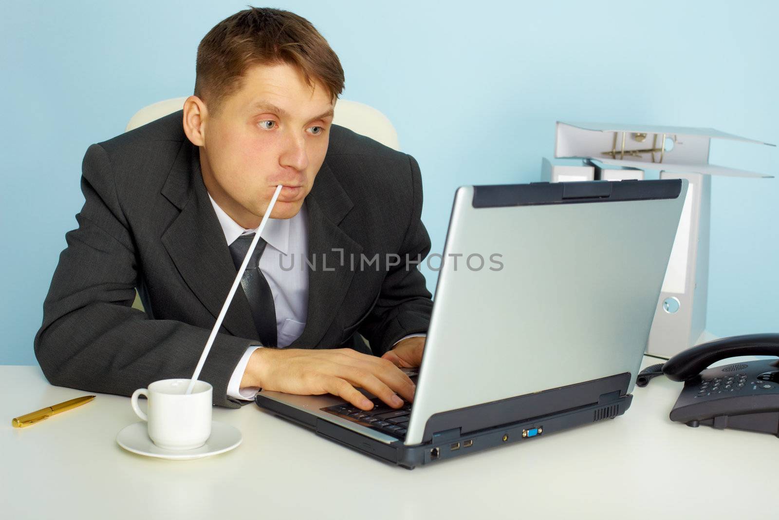 a very busy man working with laptop computer and drinks coffee through a straw
