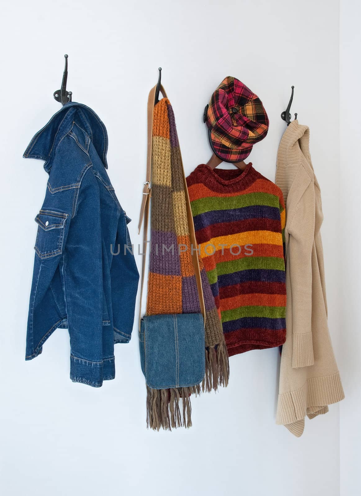 Colorful clothing and bag on metal coat hooks, on a white wall.