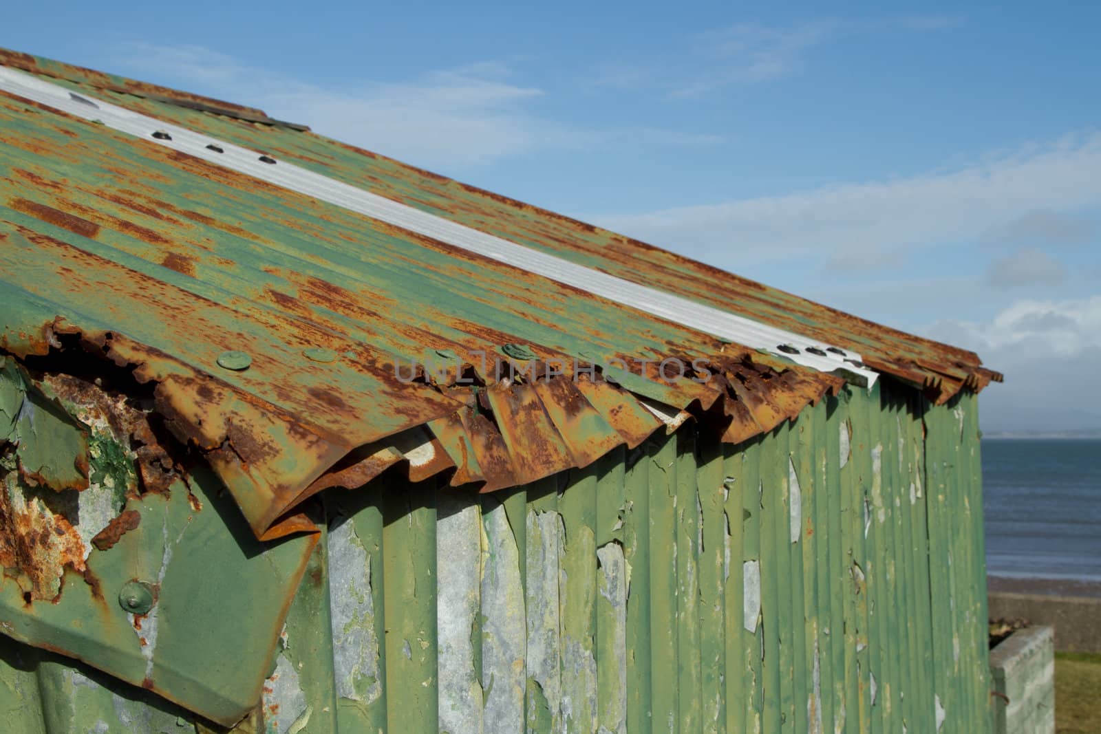 The roof of a tin hut with damaged rusty metal and green flaking paint.