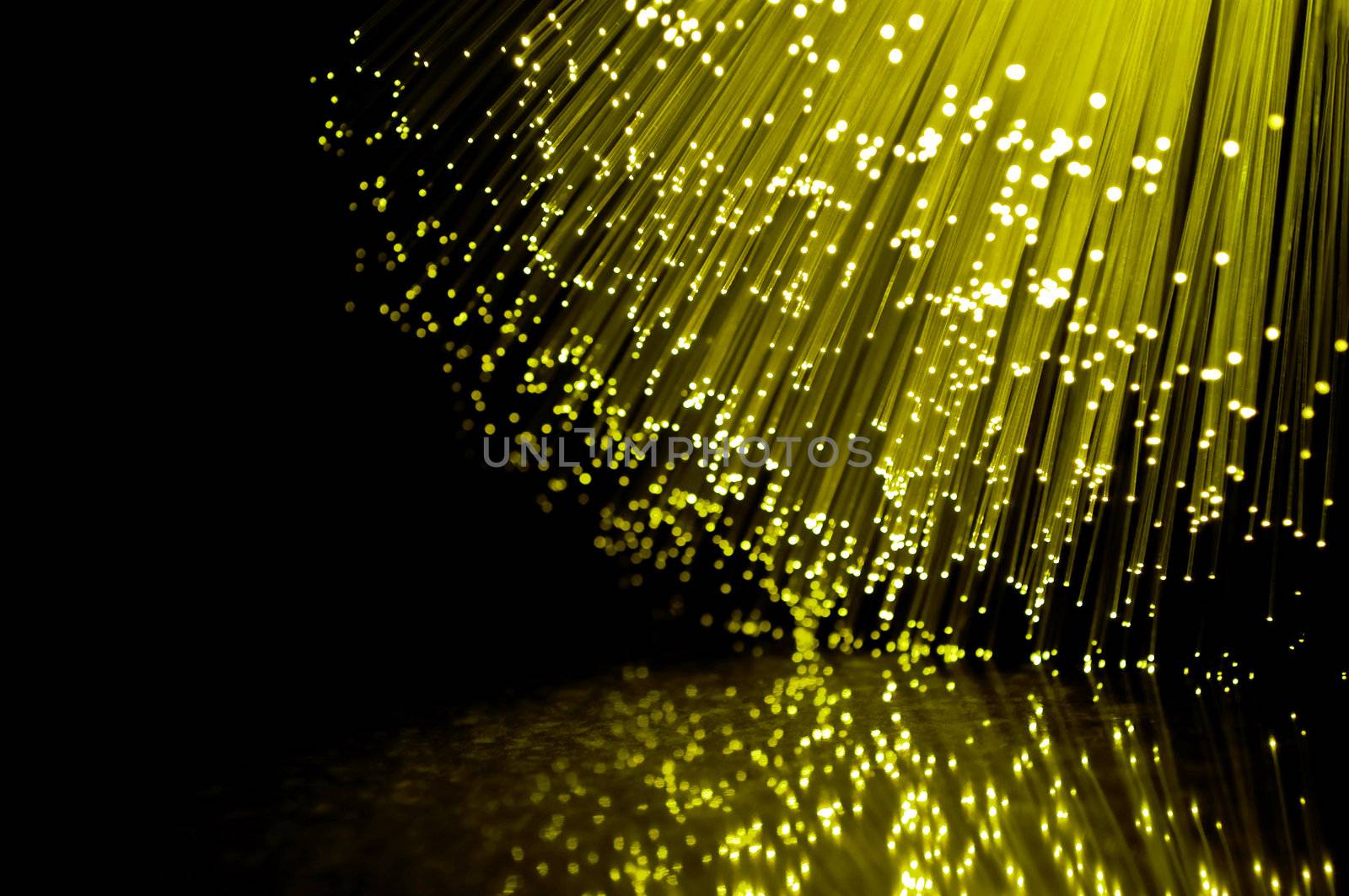 Close up on the ends of many illuminated fibre optic strands against black and reflecting into foreground.