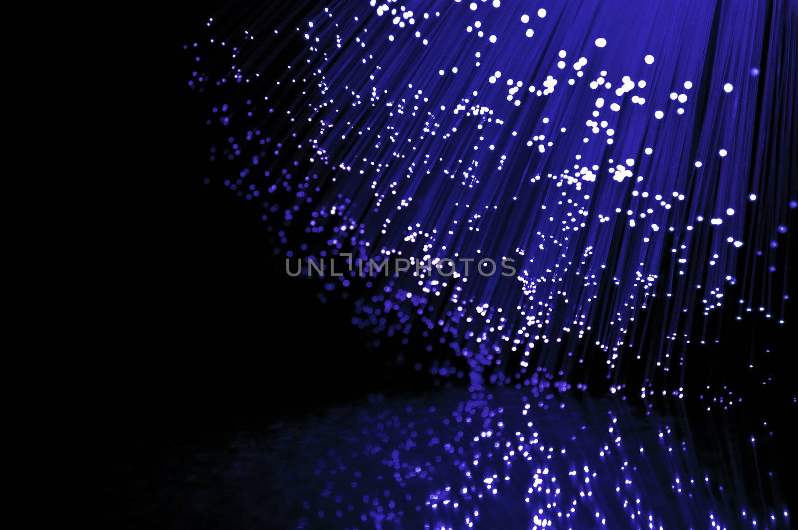 Close up on the ends of many illuminated fibre optic strands against black and reflecting into foreground.