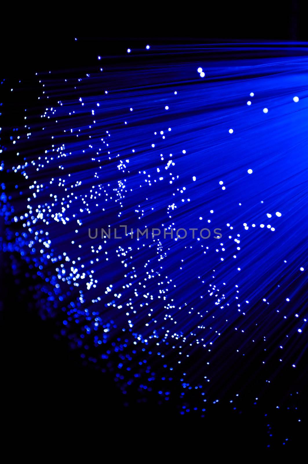 Close up on ends of many illuminated deep blue fibre optic strands with black background.