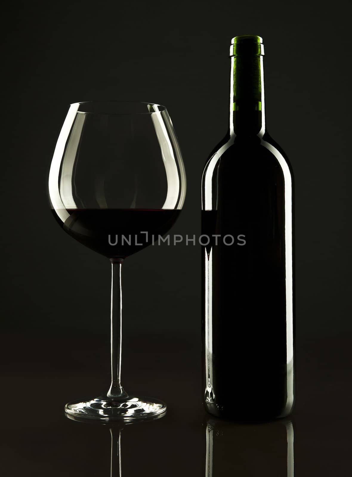 A bottle of red wine and a glass with it on a dark black background