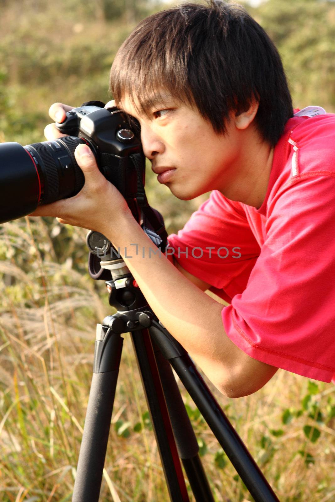 photographer with the camera on a tripod. On a background yellow grass