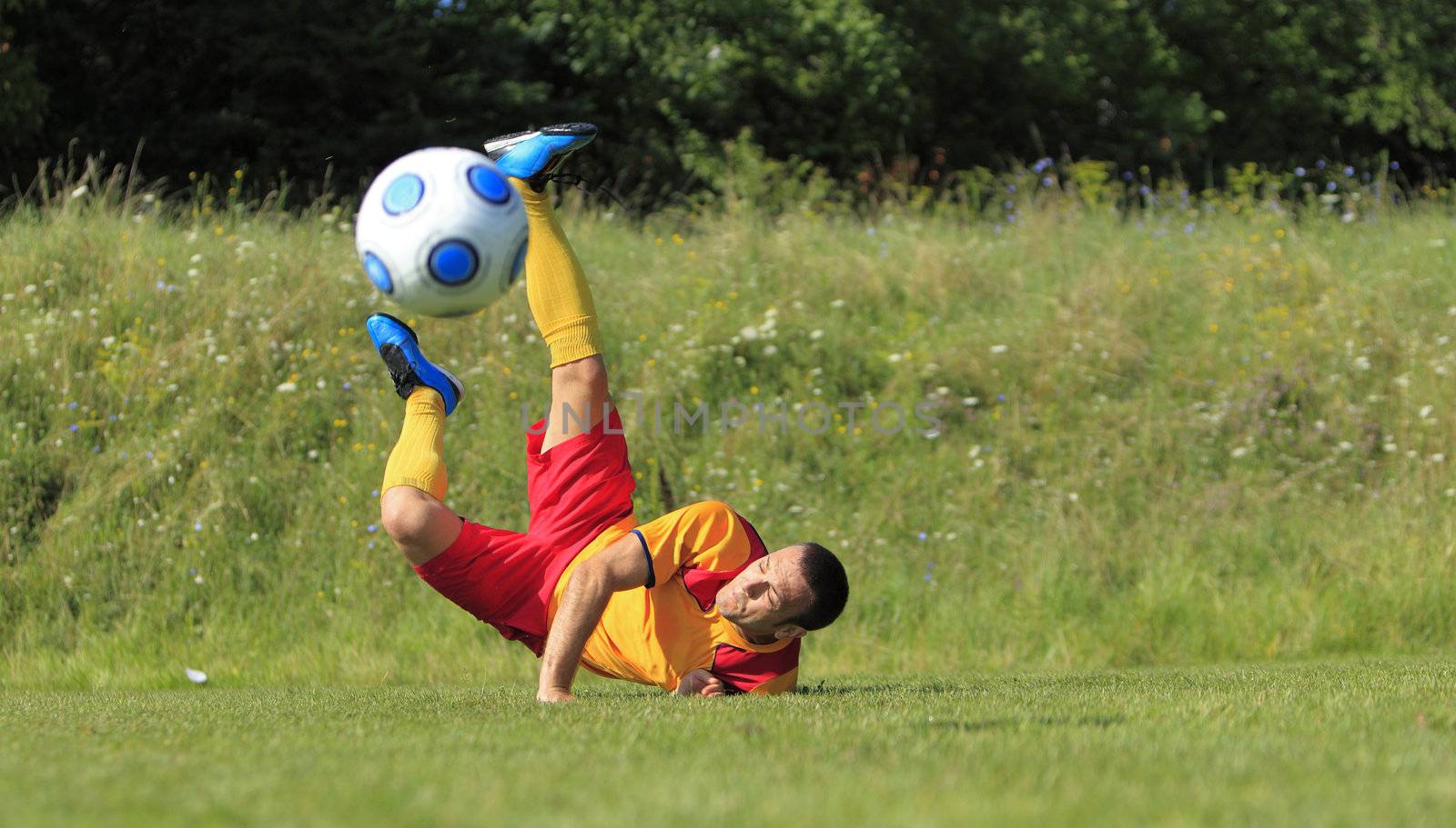 A soccer player on the ground after he kicked the ball in an acrobatic position.