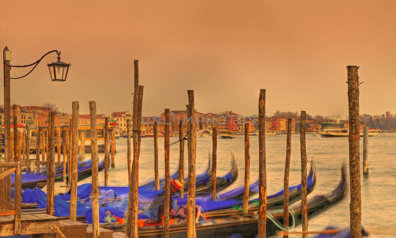 Sunset colors in Venice with gondolas in first plane and specific architecture in the distance.