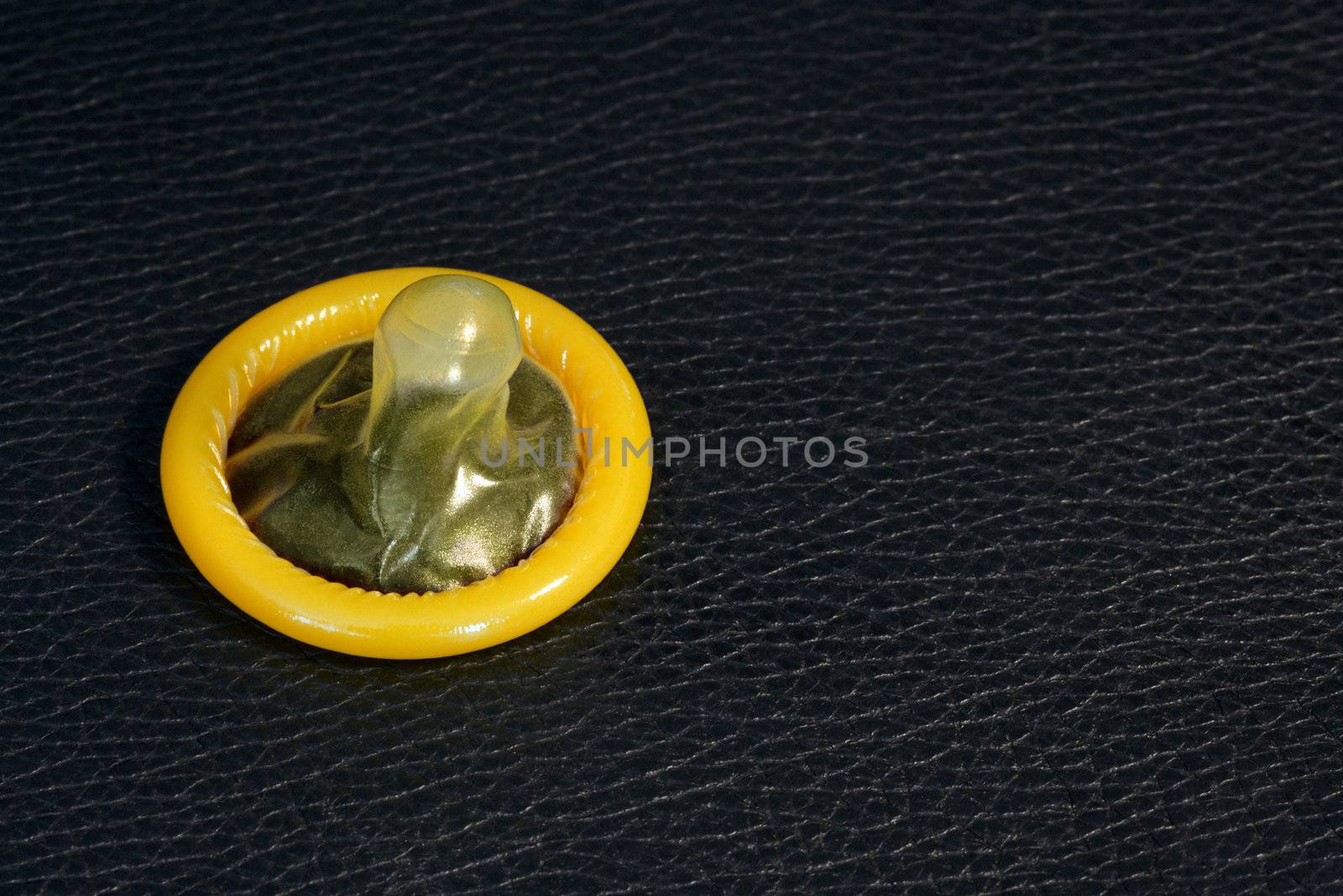 Image of a yellow condom on black leather.
