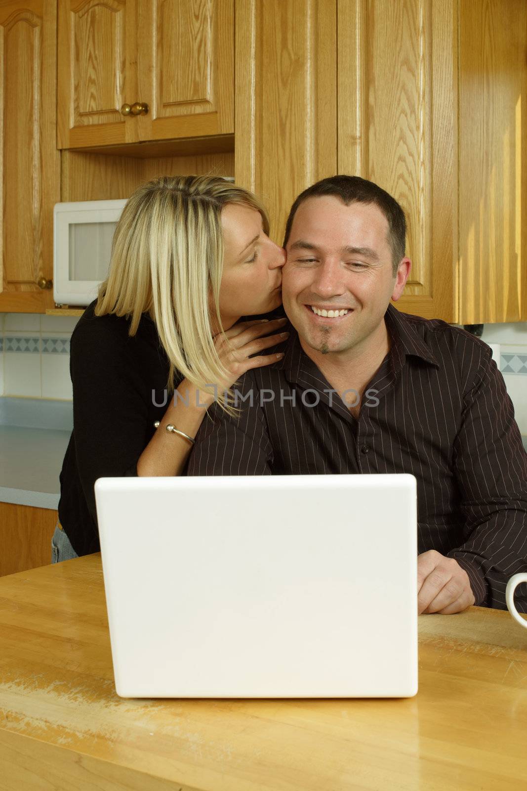 A loving couple, searching the internet on their laptop in their kitchen.
