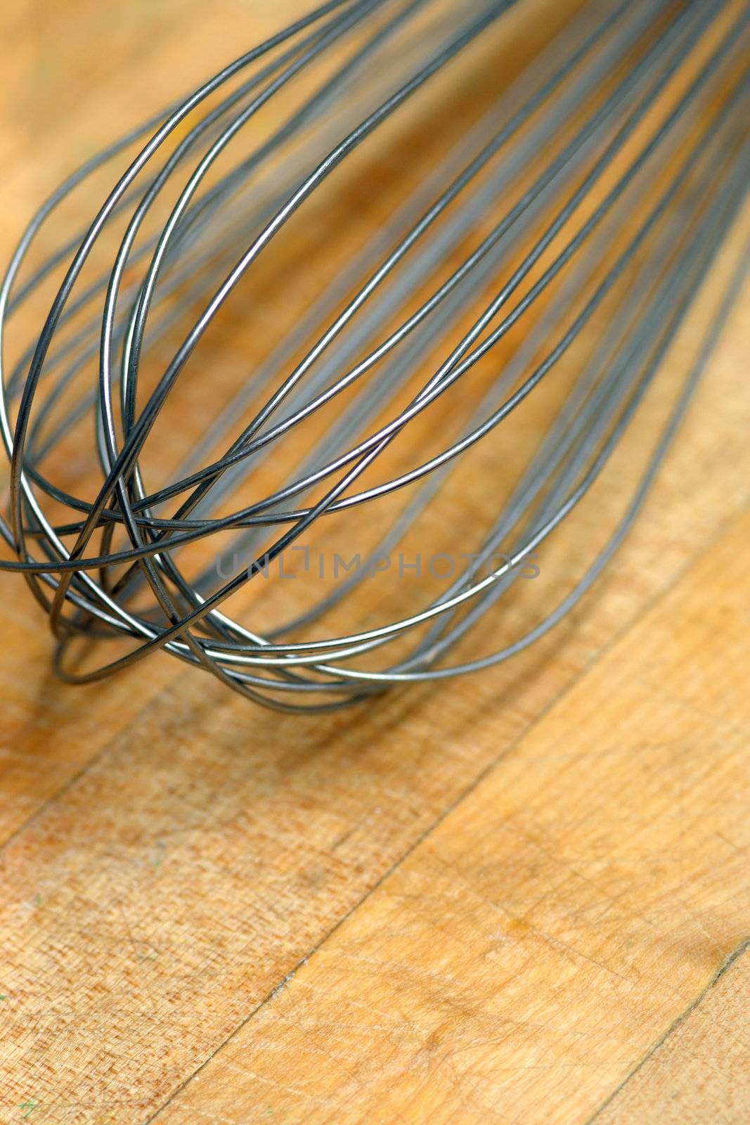 Wire whisk resting on a well worn cutting board of a commercial bakery.  Shallow depth of field.
