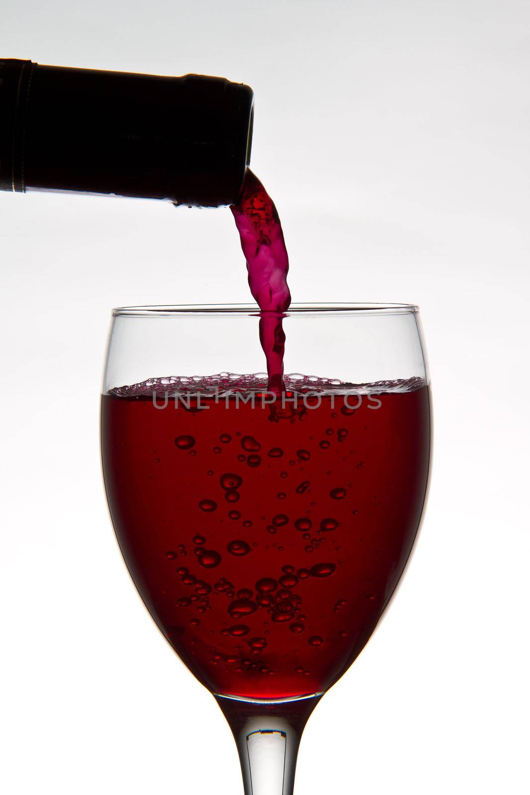 red wine pouring down from a wine bottle into a wine glass on white background
