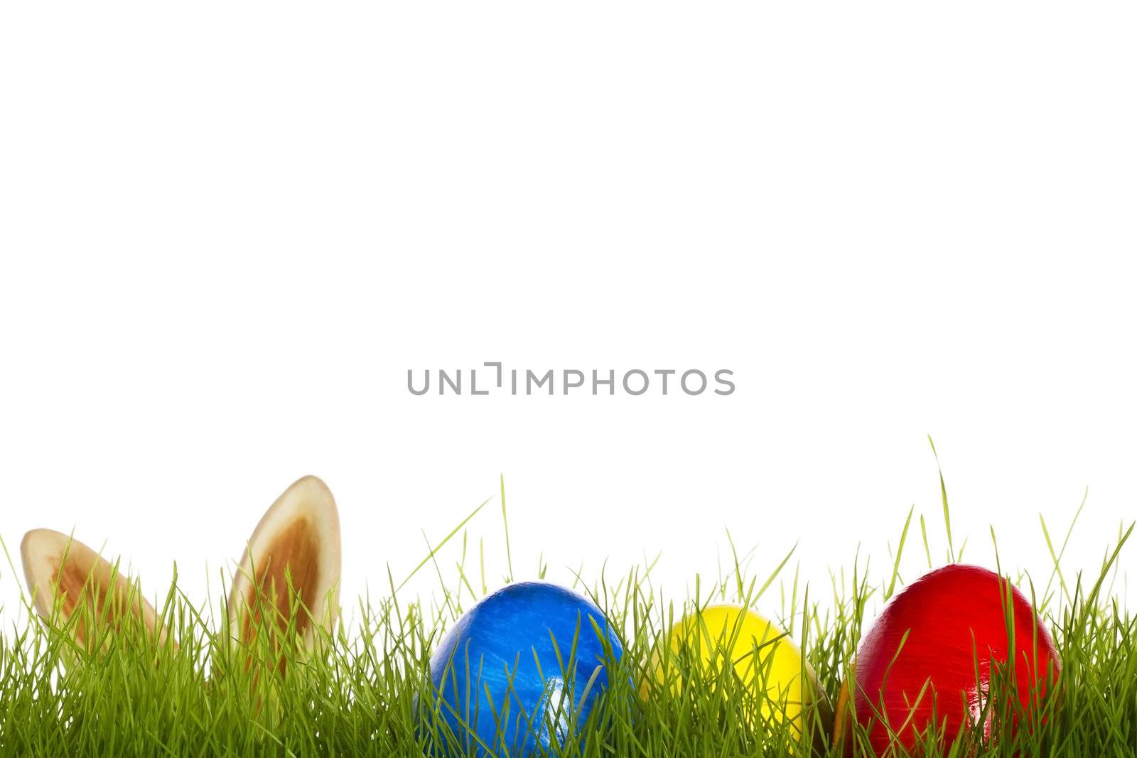 three easter eggs in grass with ears from a easter bunny in background on white