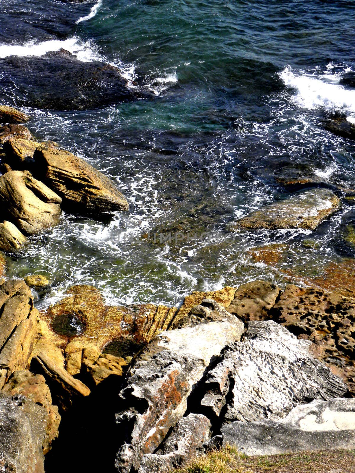 Photo presents rocks and foamy ocean.