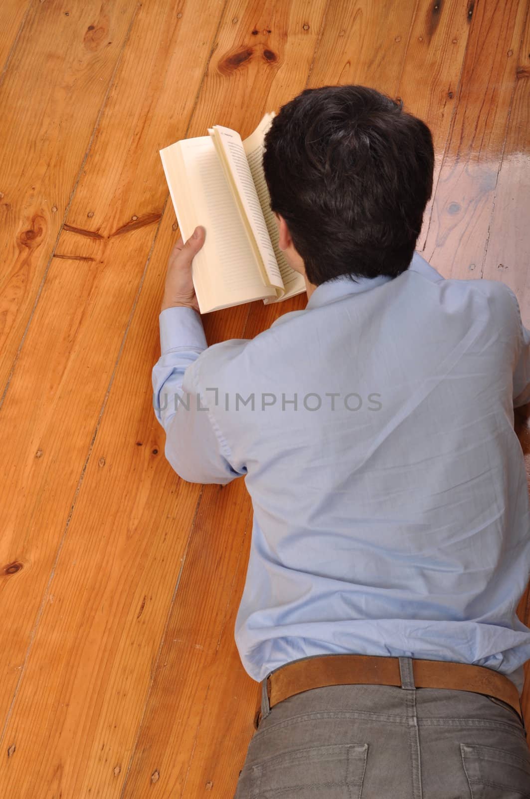 back view of a young man reading a business book while lying on the floor at home