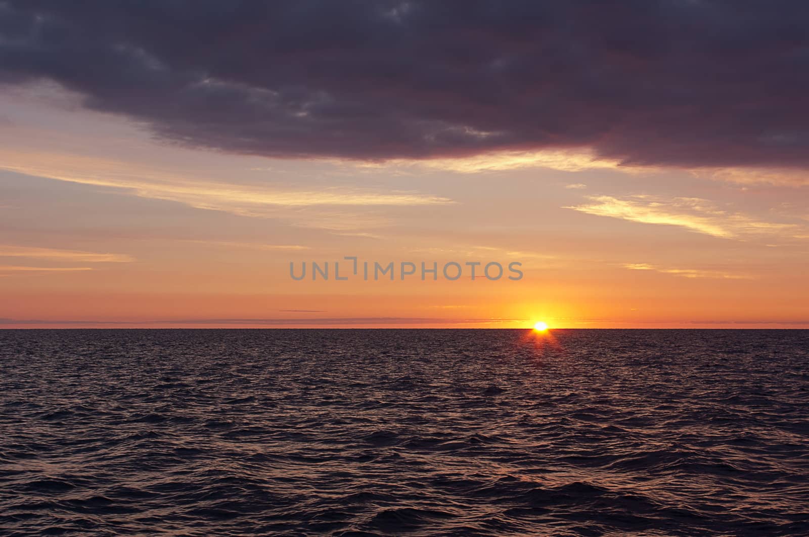 A morning sunrise over water. The sun is halfway above the horizon. 