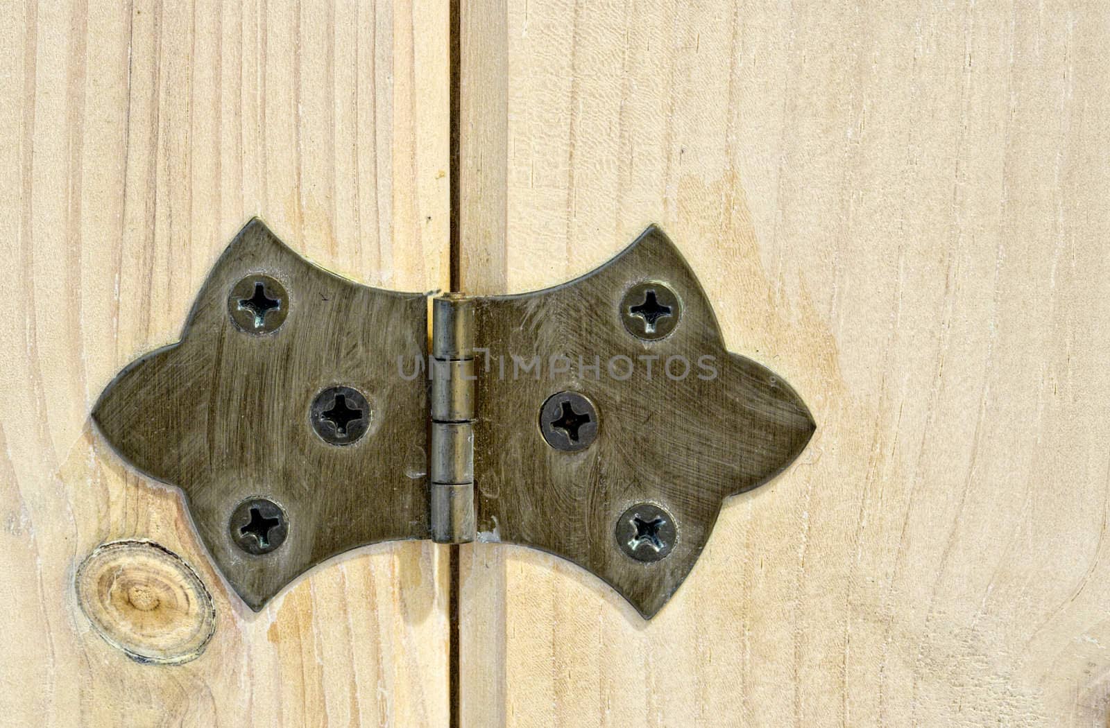 A close up view of a hinge attached to a wood cabinet door. Much detail can be seen in both the hinge and the wood.