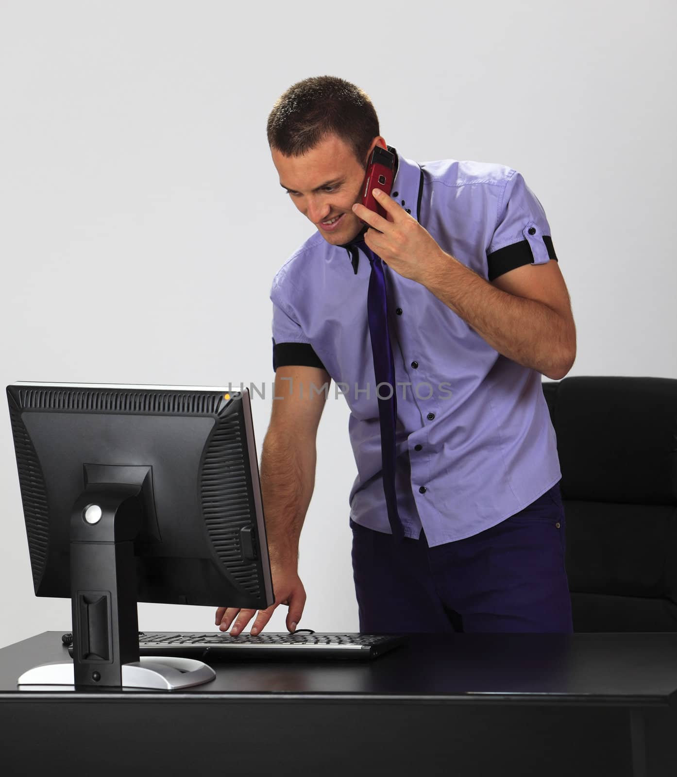 Young casual man discussing on the phone while is typing something on the keyboard in the office.