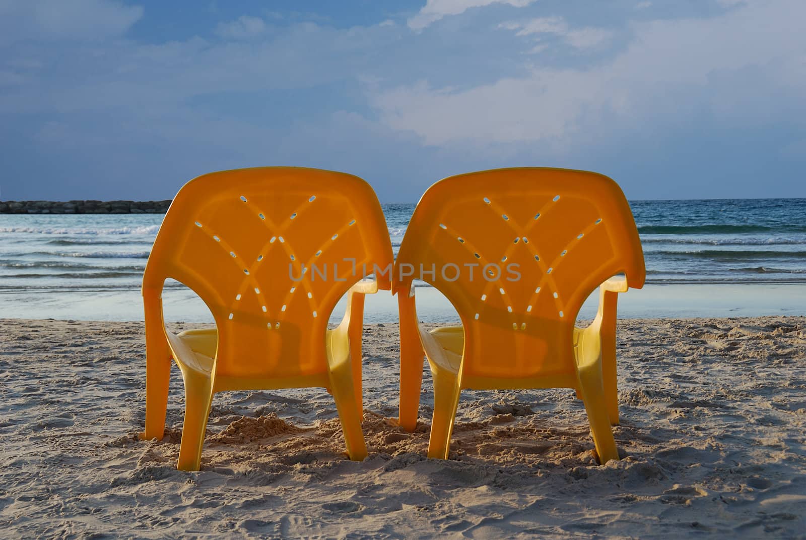 Couple of yellow plastic beach chairs standing on sand and facing to sea