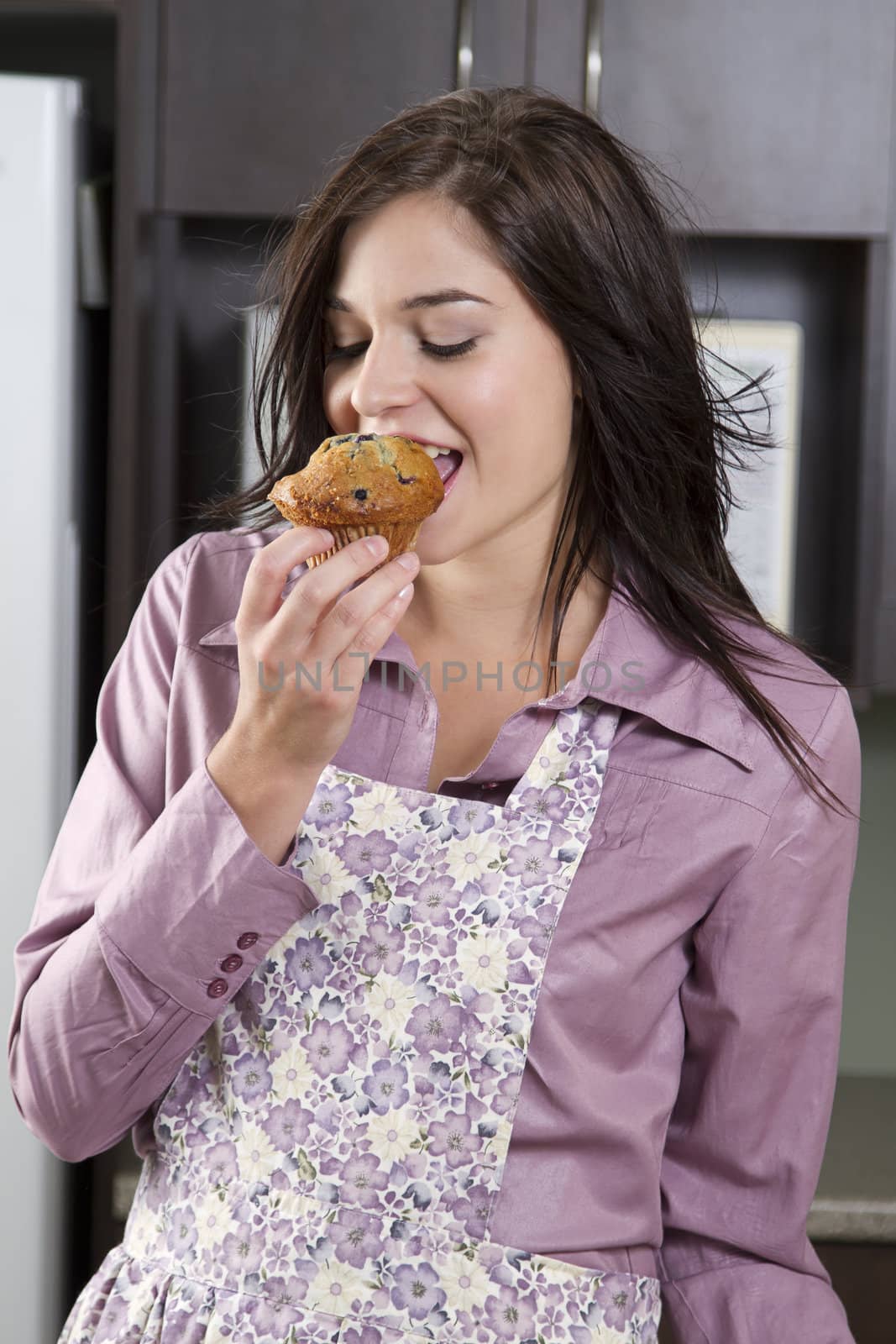 Young woman wearing an apron taking a bite blueberry muffin