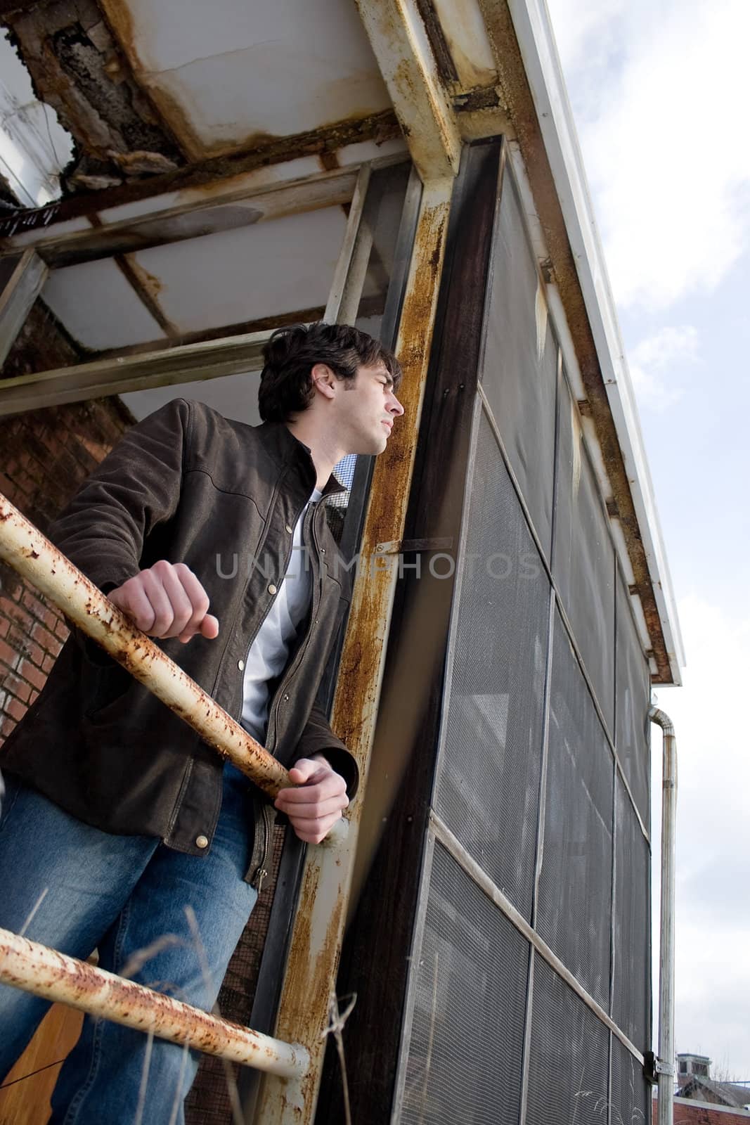 A young brunette man posing outside a worn and abandoned building.