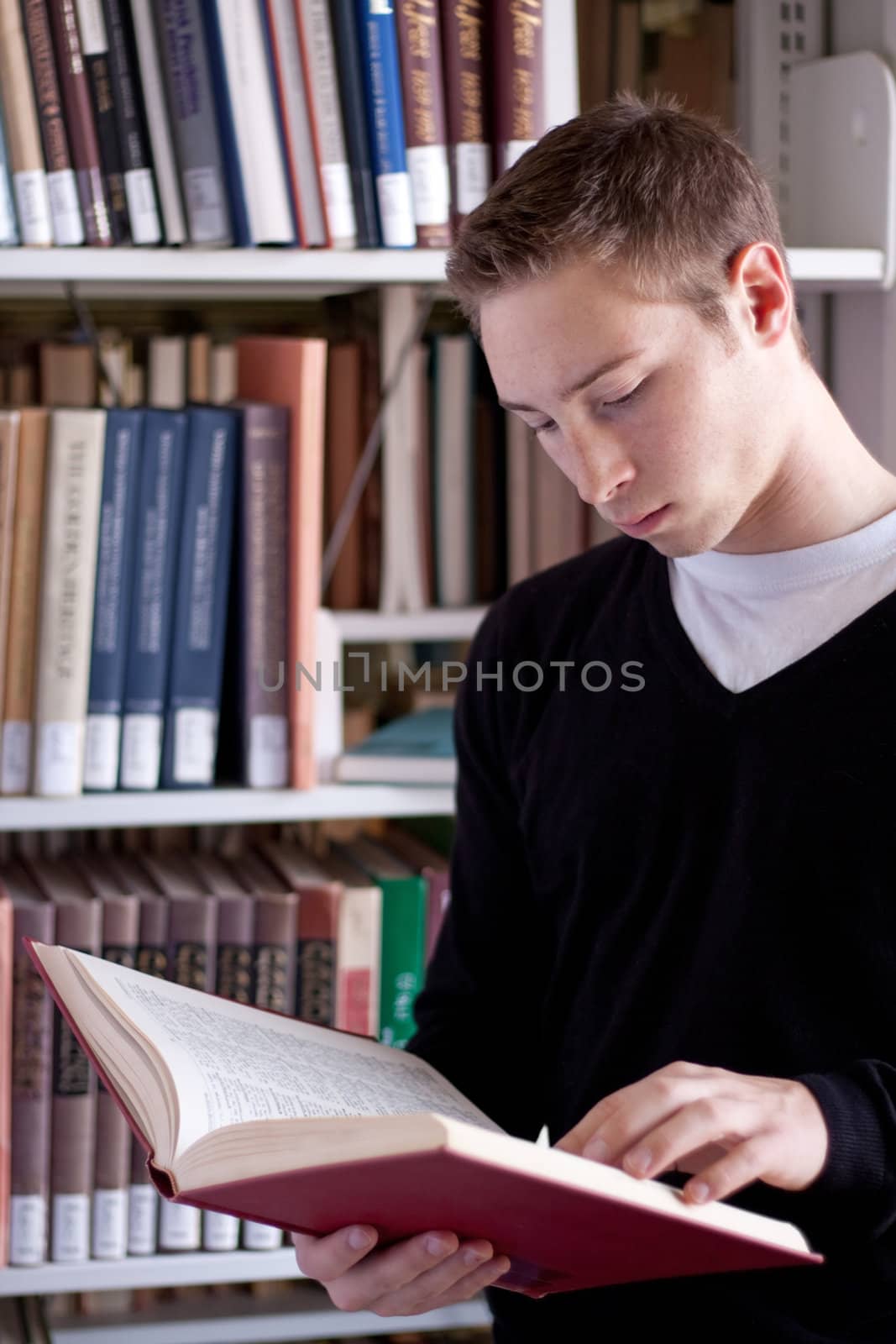 A young college aged man reading a book at the library.