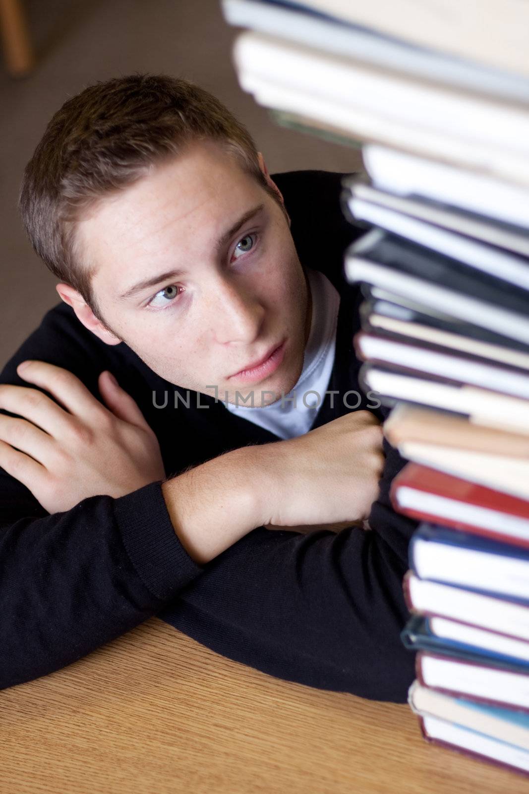 A frustrated and stressed out student looks up at the high pile of textbooks he has to go through to do his homework.