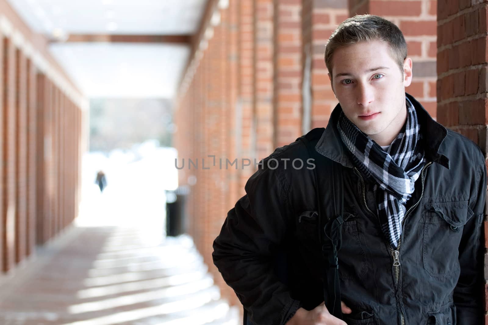 A portrait of a young man standing in an outdoor corridor with his backpack.