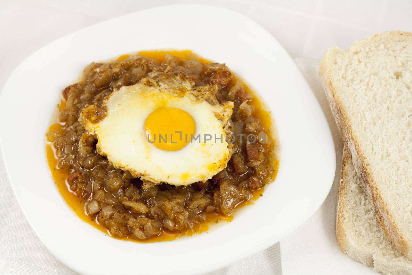 Delicious stew with baked onion, egg and sausages served on table with two slices of bread