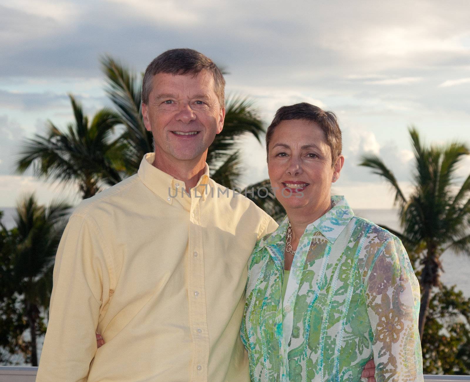 Smiling retired couple smiling as the sun sets behind over the palm lined ocean