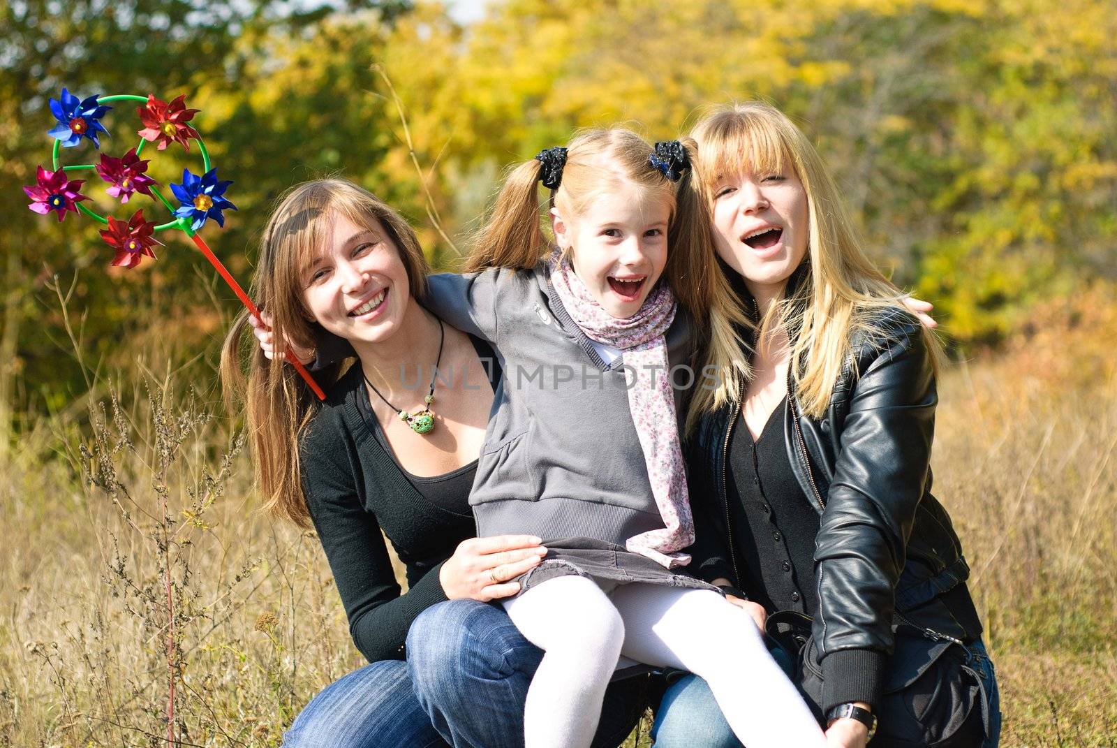 Smiling young mother, little daughter and sister outdoor. Autumn day.