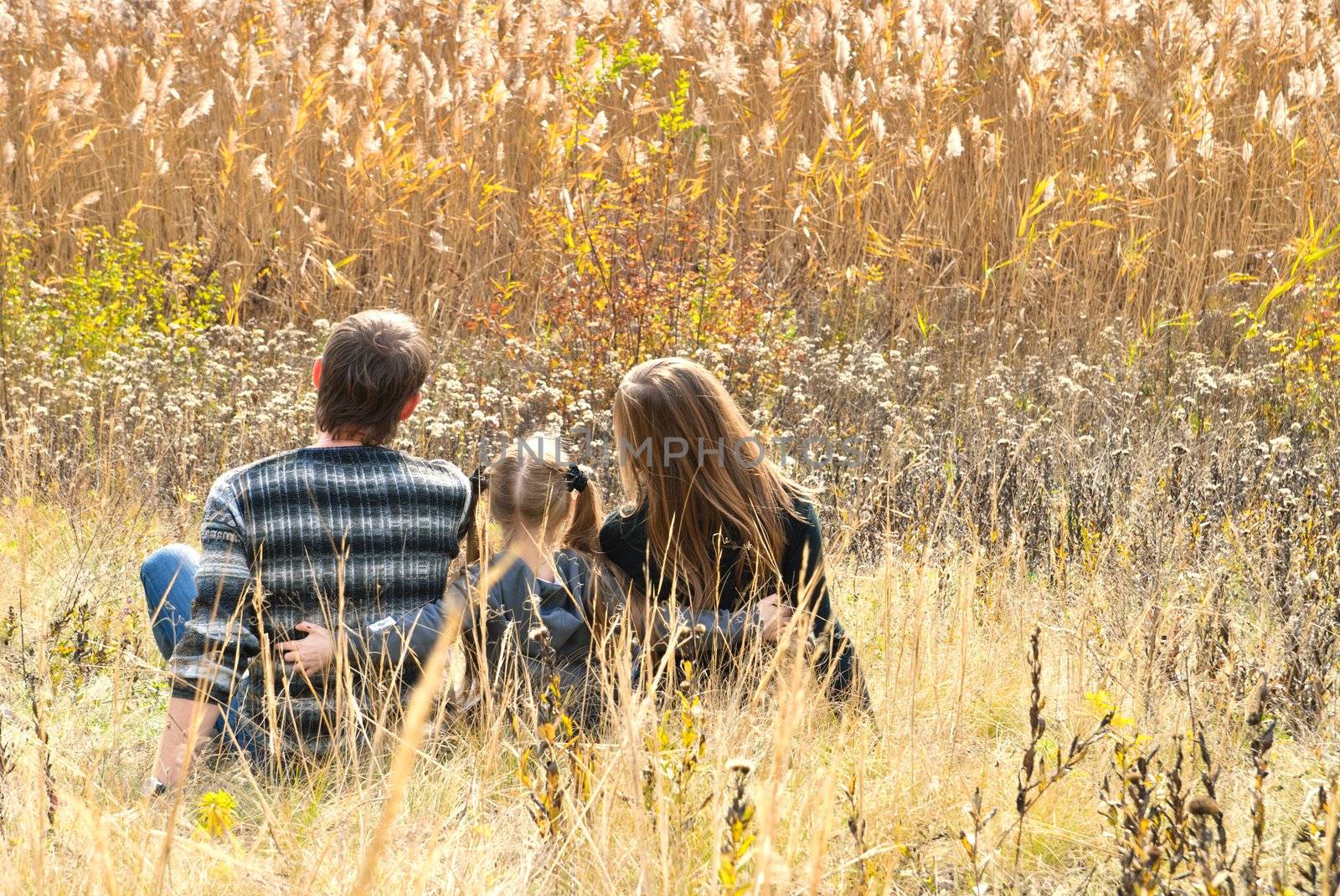 Mother, father and daughter sitting at the meadow in autumn