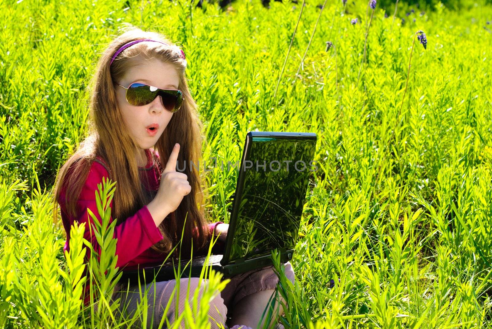 Smiling little girl with laptop outdoor. Sunny summer day.