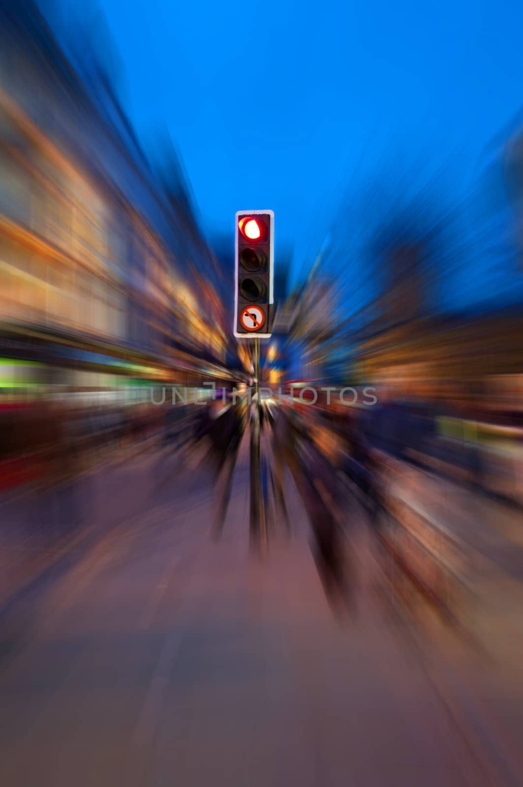 A traffic light surrounded by radial motion blur giving a chaotic concept to an evening urban street.