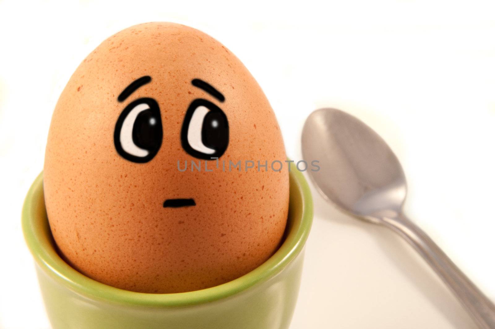 Close up of boiled egg with comic painted face looking worried about the spoon to the side. White background.