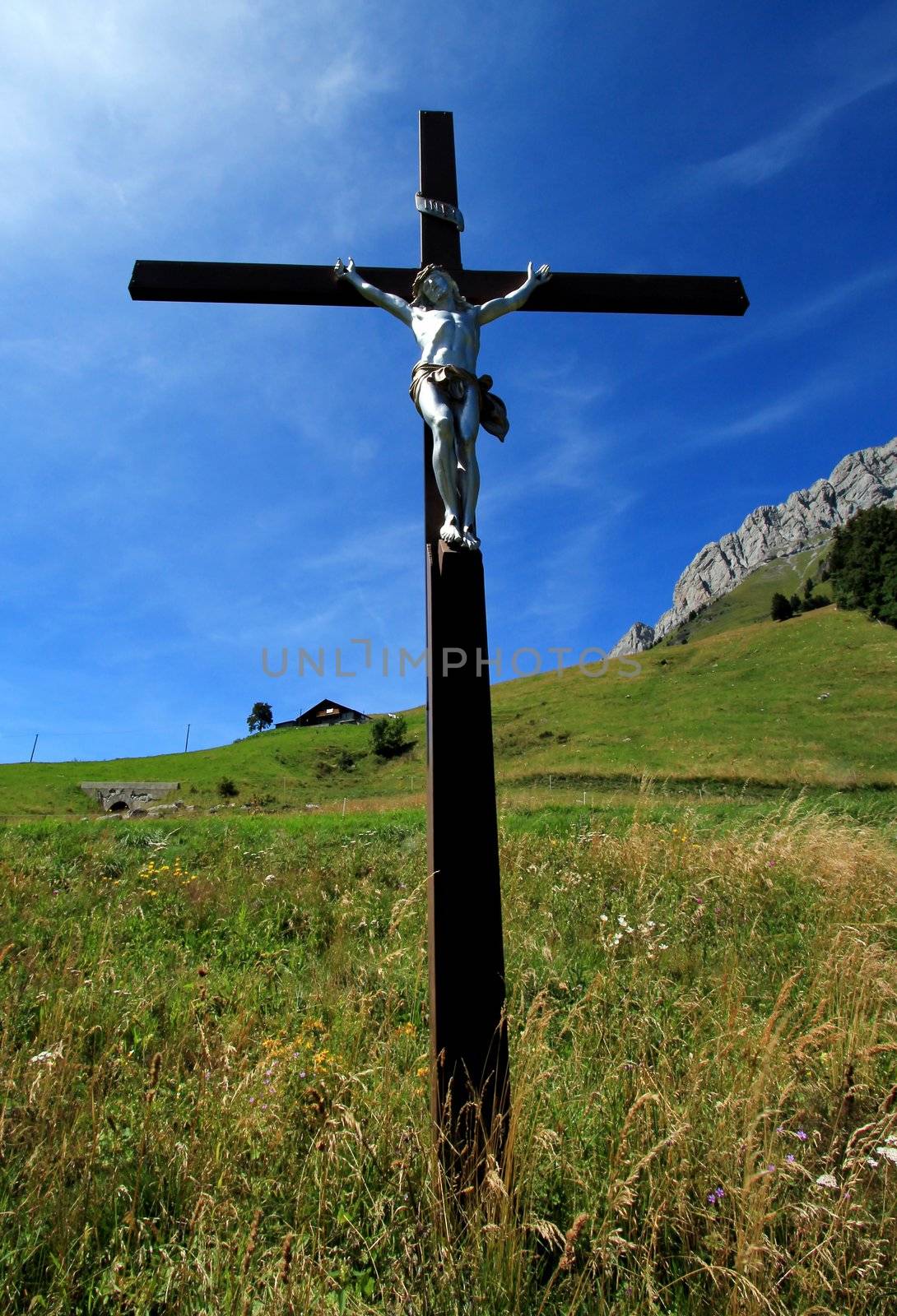 White sculpture of Jesus on a wood cross in the green mountain by summer