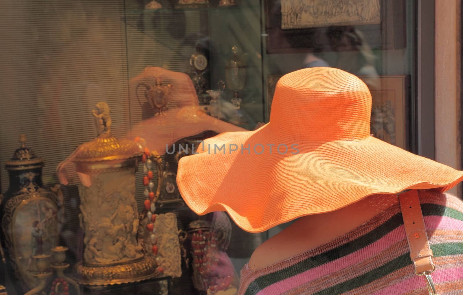 Image of an old lady with a big orange hat looking to an antique window shop in Venice,Italy.