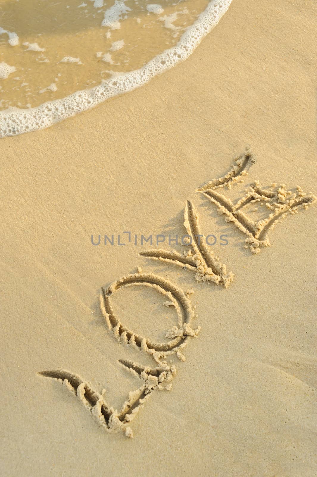 Inscription "love" on sand. Sea coast with a rolling wave on an inscription