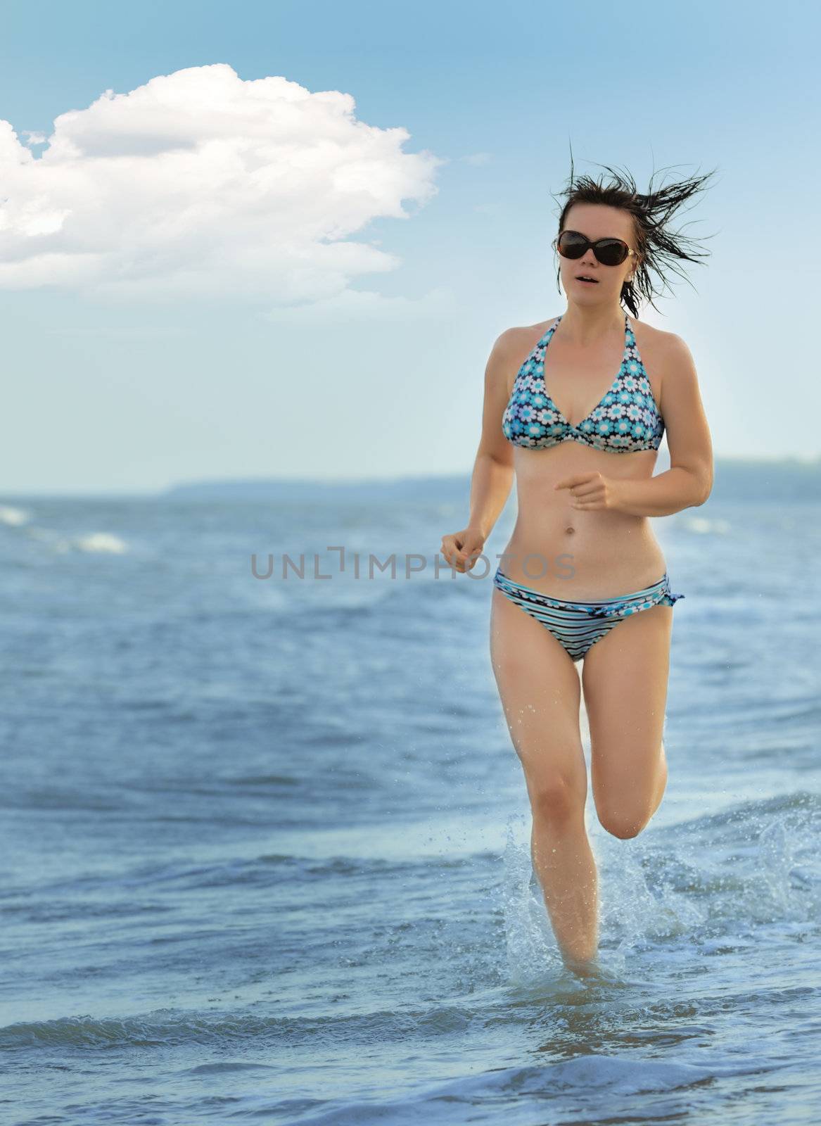 The girl running on seacoast. The European appearance in sunglasses