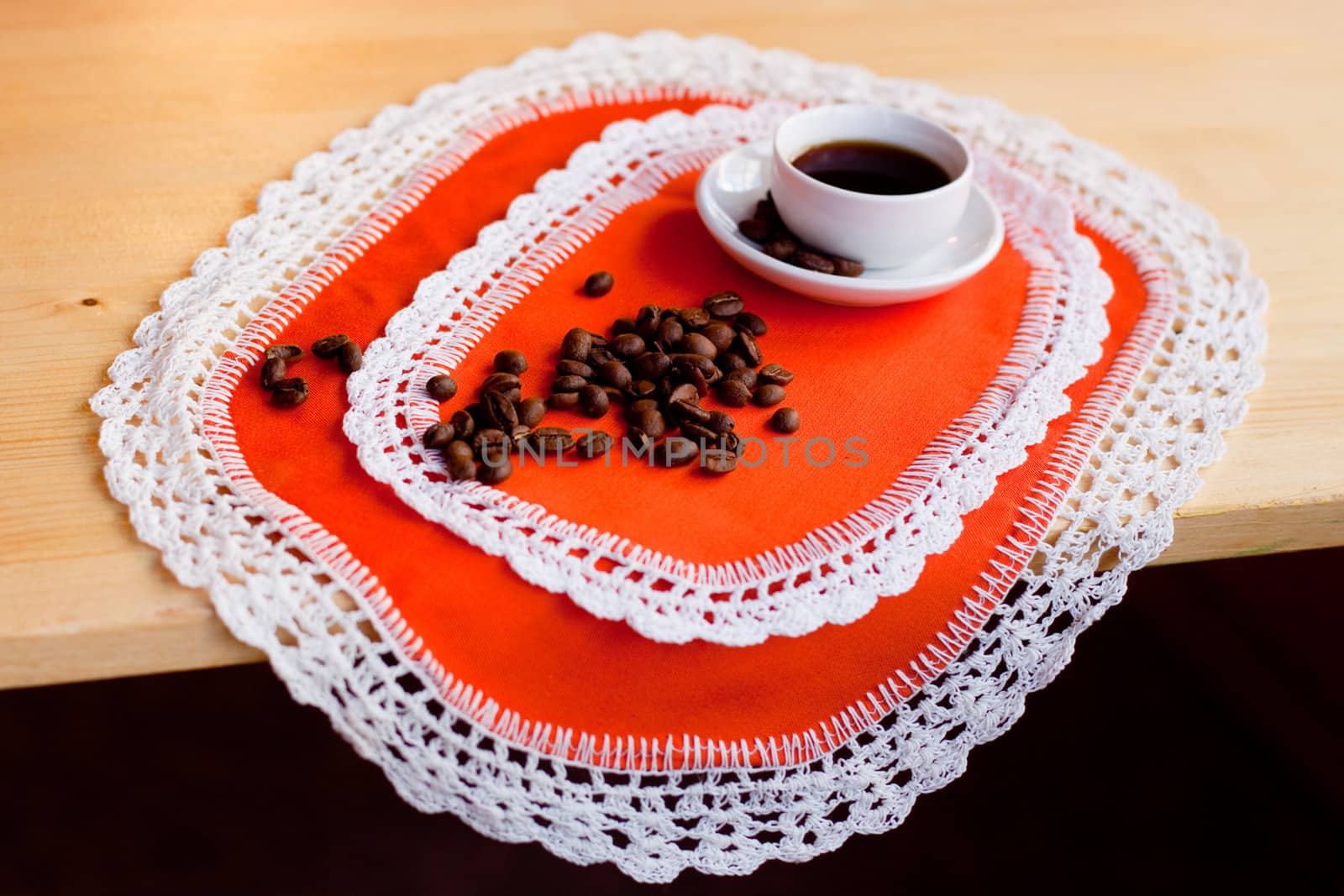 A coffee cup and coffee beans on two orange napkins
