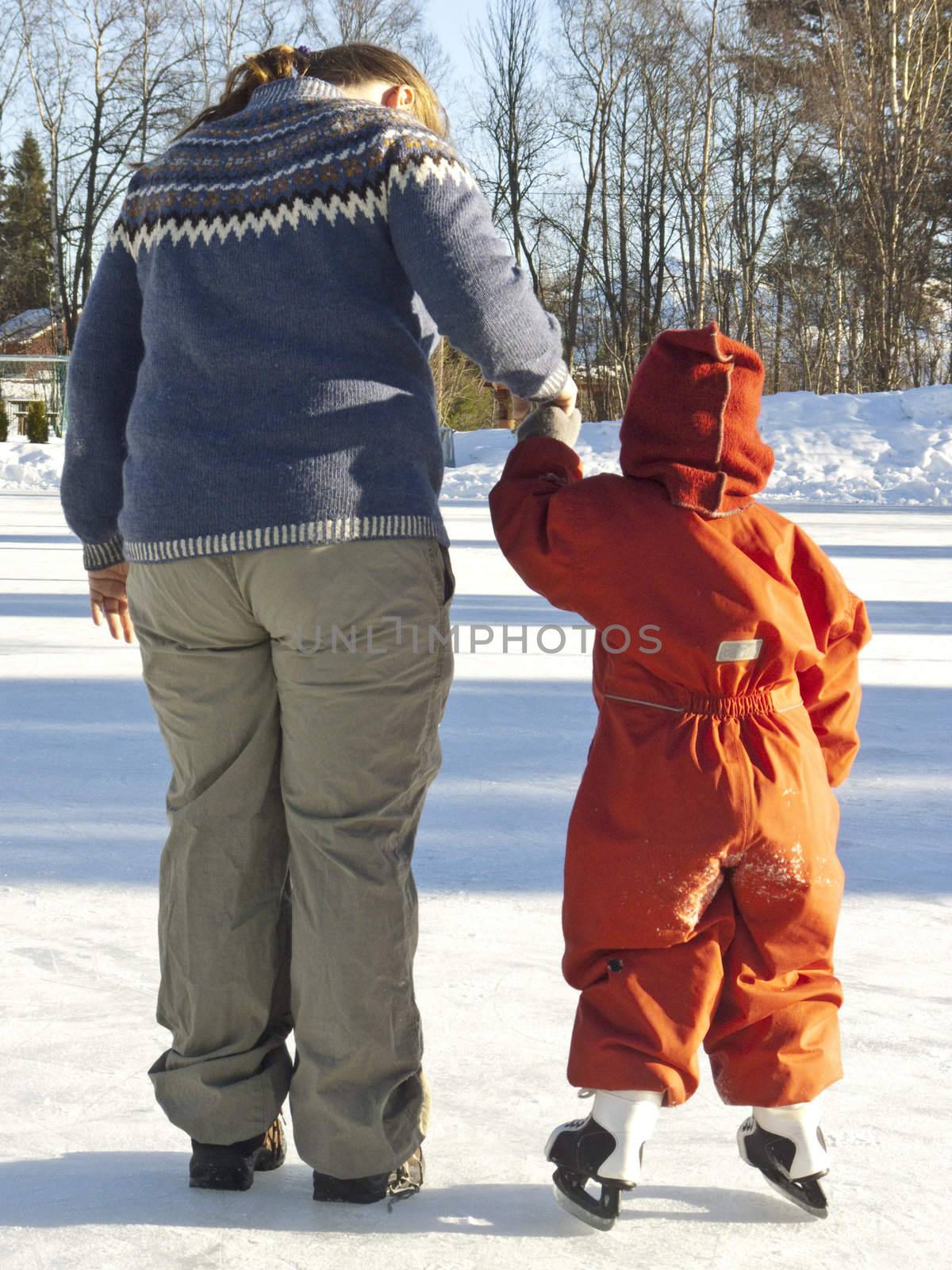 Small child (3 years old) learning to ice skate, holding her mother's hand